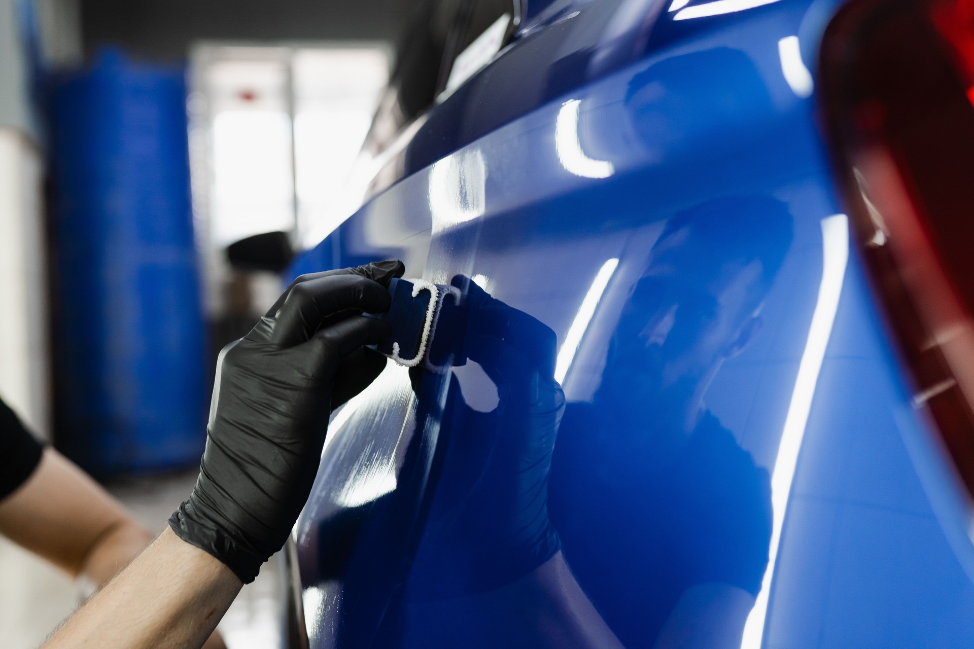 Process of applying ceramic protective coat on body car using sponge in detailing auto service. Car service worker apply ceramic coating to protect the car body from scratches.